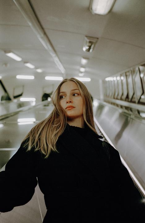 A woman with long blonde hair looks to her right while riding an escalator.