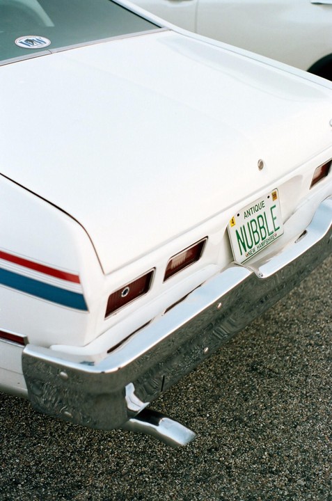 The rear of a white car with a New Hampshire license plate that reads "NUBBLE" is parked on asphalt.