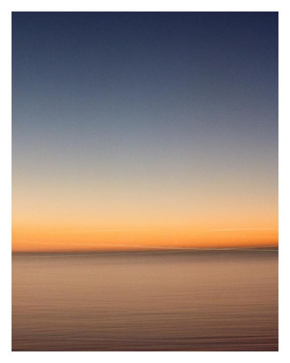 The horizon separates a dark blue sky from a body of water reflecting the orange glow of the sunset.