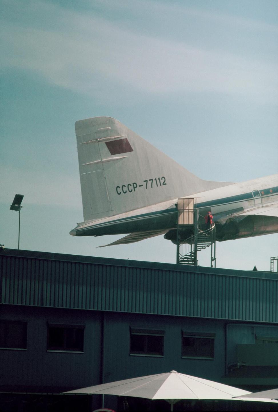 A large airplane with "CCCP-77112" written on its tail is displayed above a building, with a person on a spiral staircase leading to the plane.