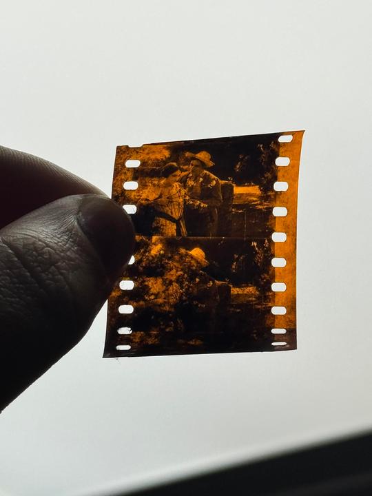 A person holds up a strip of film showing a couple standing outdoors.