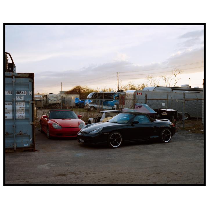 Two sports cars are parked next to a shipping container in an industrial area.