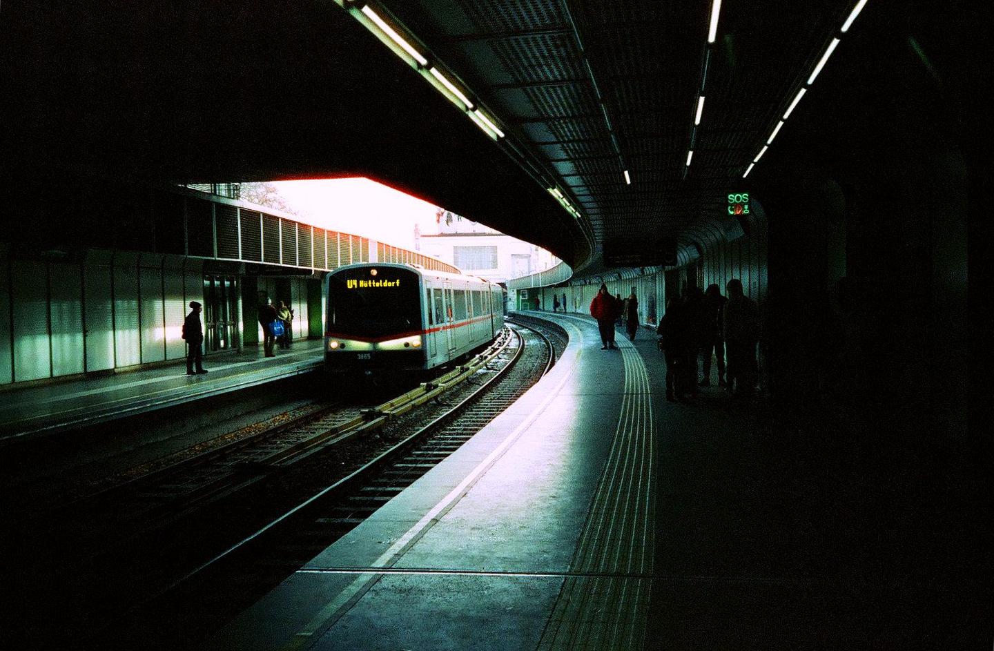A metro train is arriving at a station with people waiting on the platform.