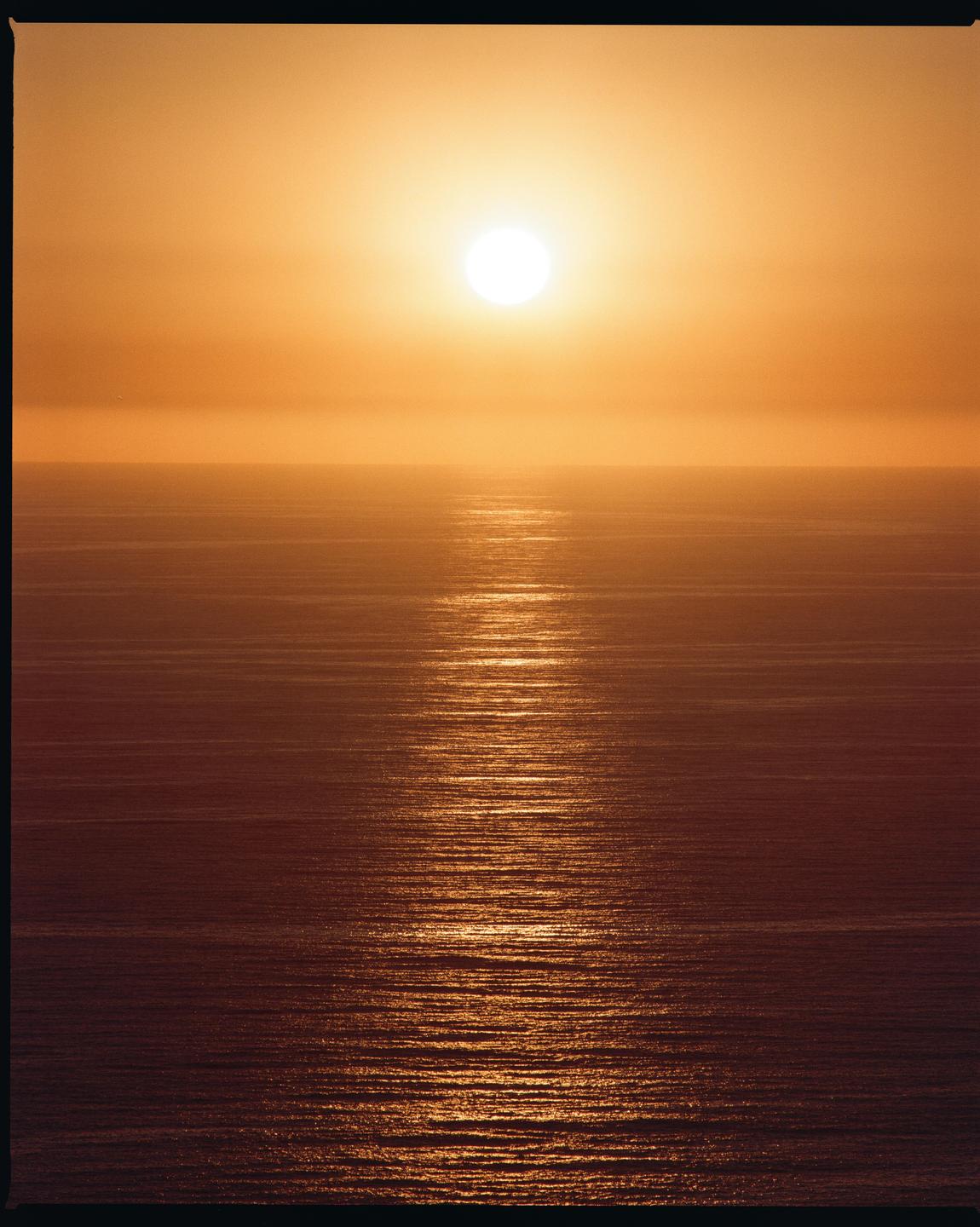 The sun sets over the ocean, creating a bright reflection on the water.