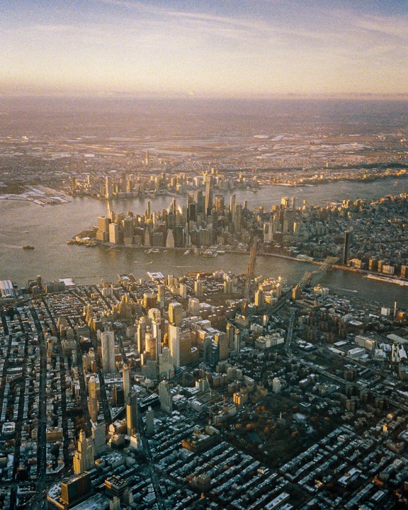 An aerial view shows the cityscape of New York with many buildings and a river.
