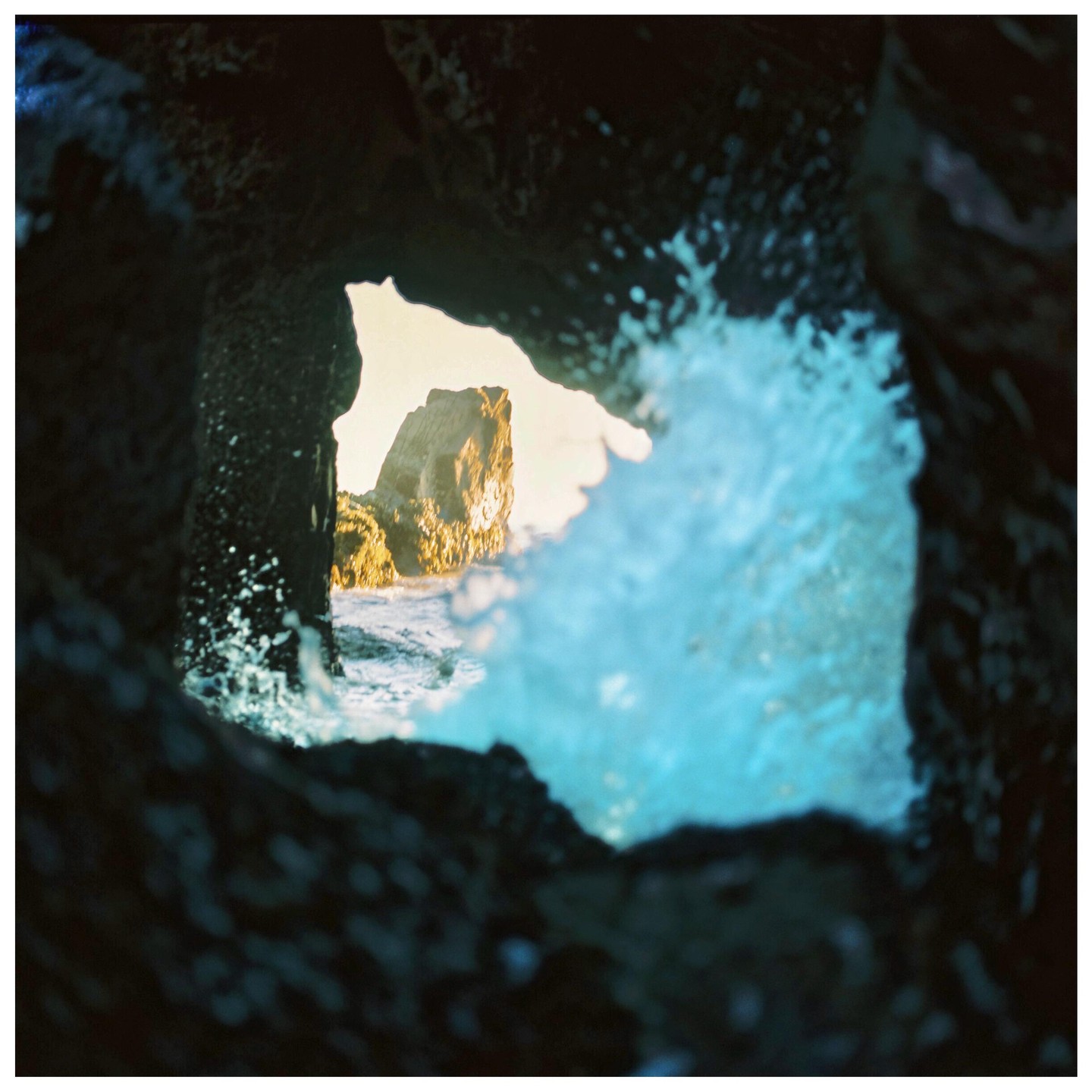 A rock formation is visible through a dark cave opening with splashing water in the foreground.