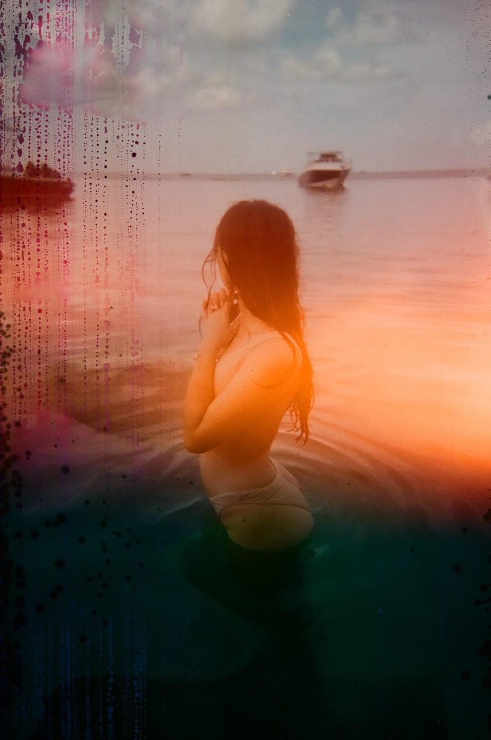 A woman stands in water with a boat in the background, with light leaks and water damage on the image.