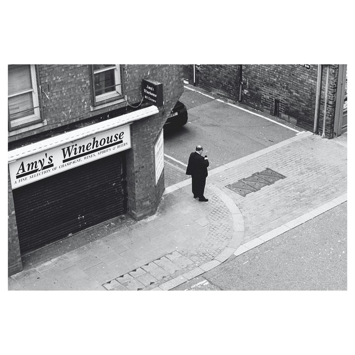 A man stands on a street corner next to a building with a sign for Amy's Winehouse.