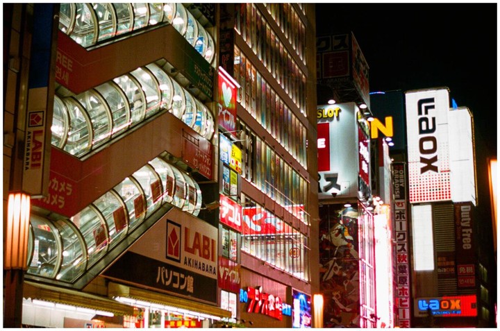 A building with multiple escalators on its exterior is illuminated by neon signs at night.