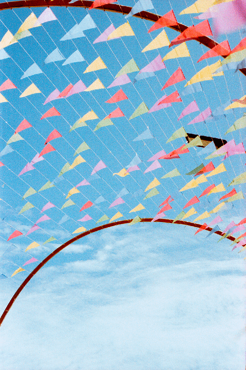 Colorful triangular flags are strung across a bright blue sky, with a brown arch visible at the bottom.
