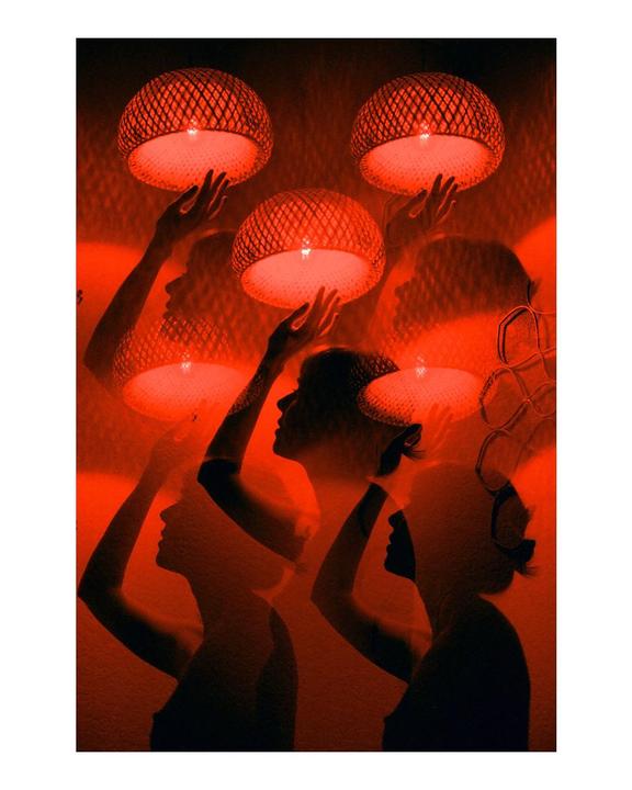 Multiple silhouettes of women are visible, some holding glowing woven lamps, against a red background.