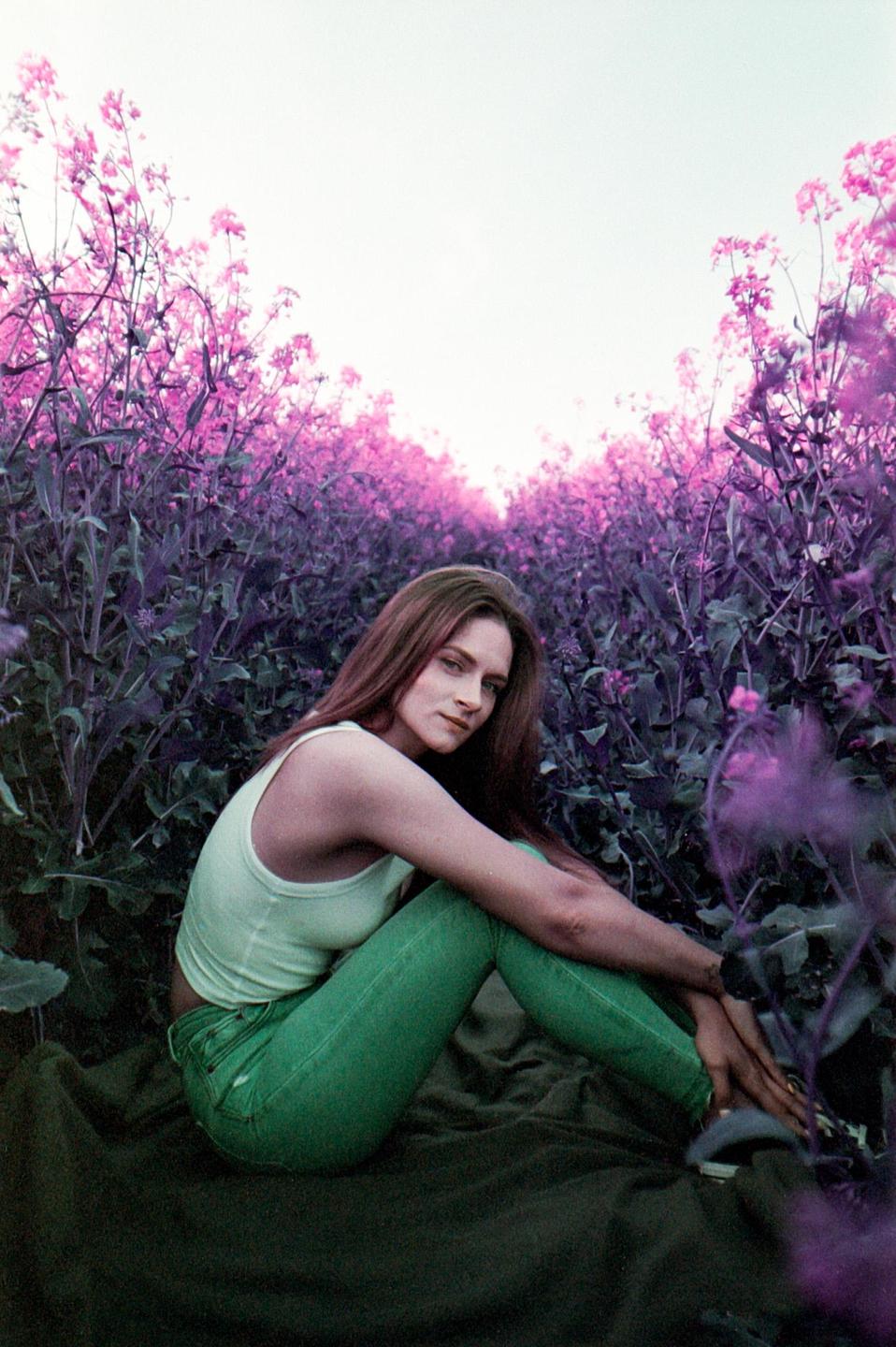 A woman sits on a blanket in a field of purple flowers.