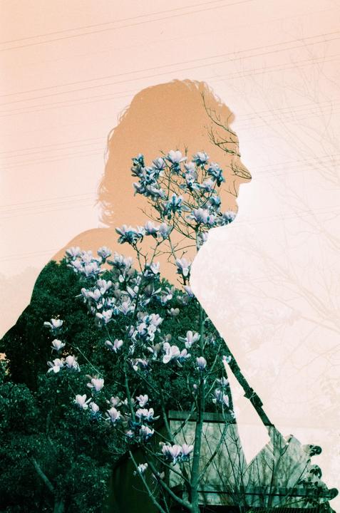 A double exposure shows the silhouette of a man overlaid with a flowering tree and green foliage.