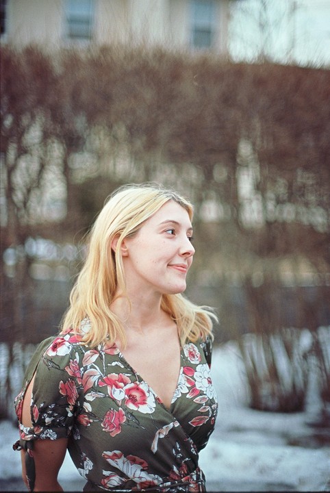 A woman with blonde hair and a floral dress smiles while looking to the right.