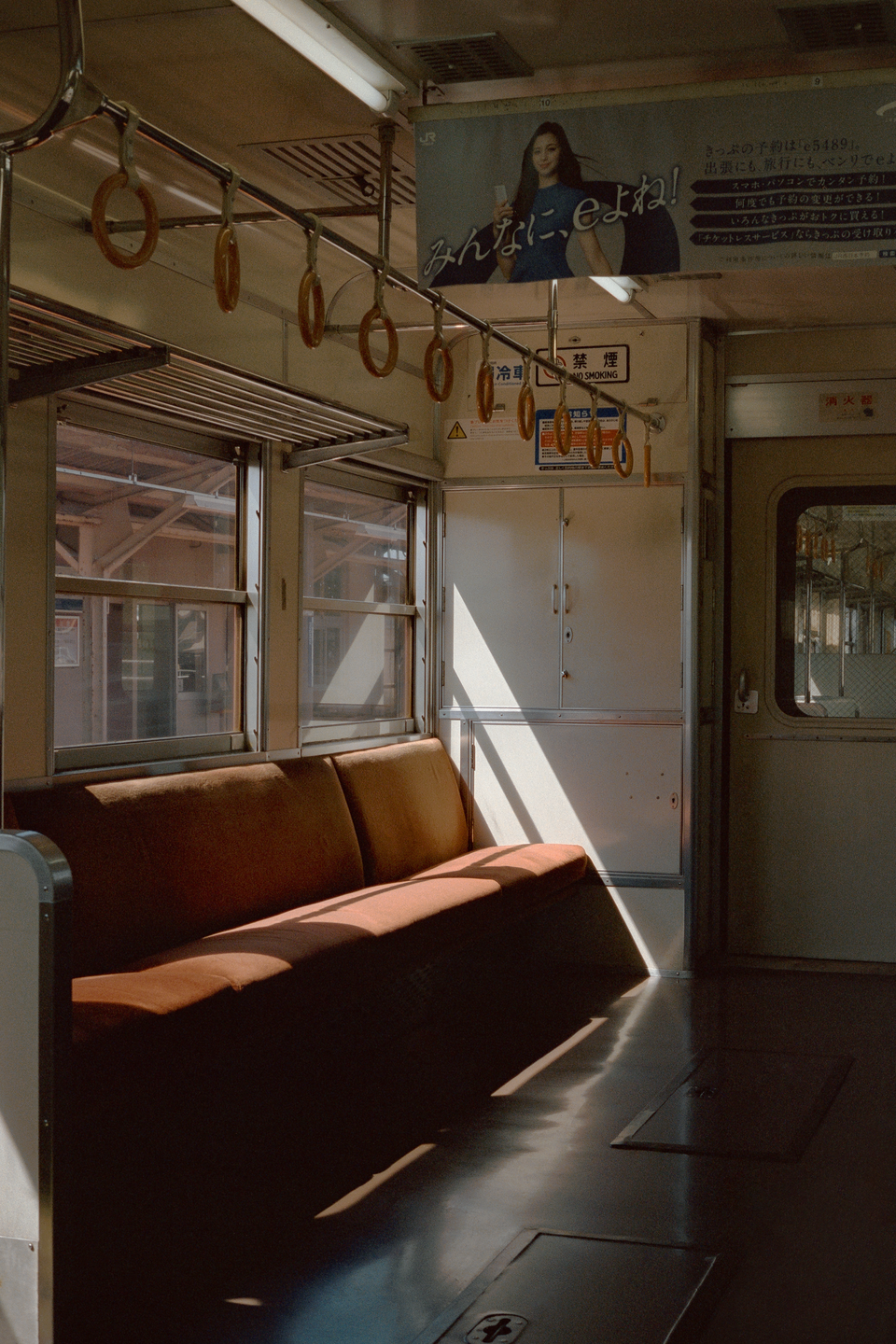 Sunlight streams through the windows of an empty train car, illuminating the brown seats and floor.