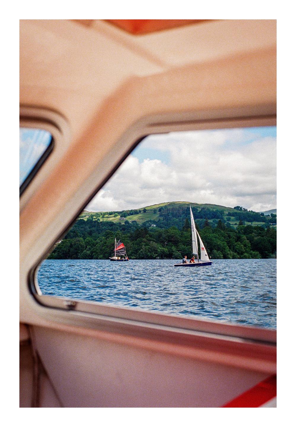 Two sailboats are visible on a lake through a window, with a forested hill in the background.