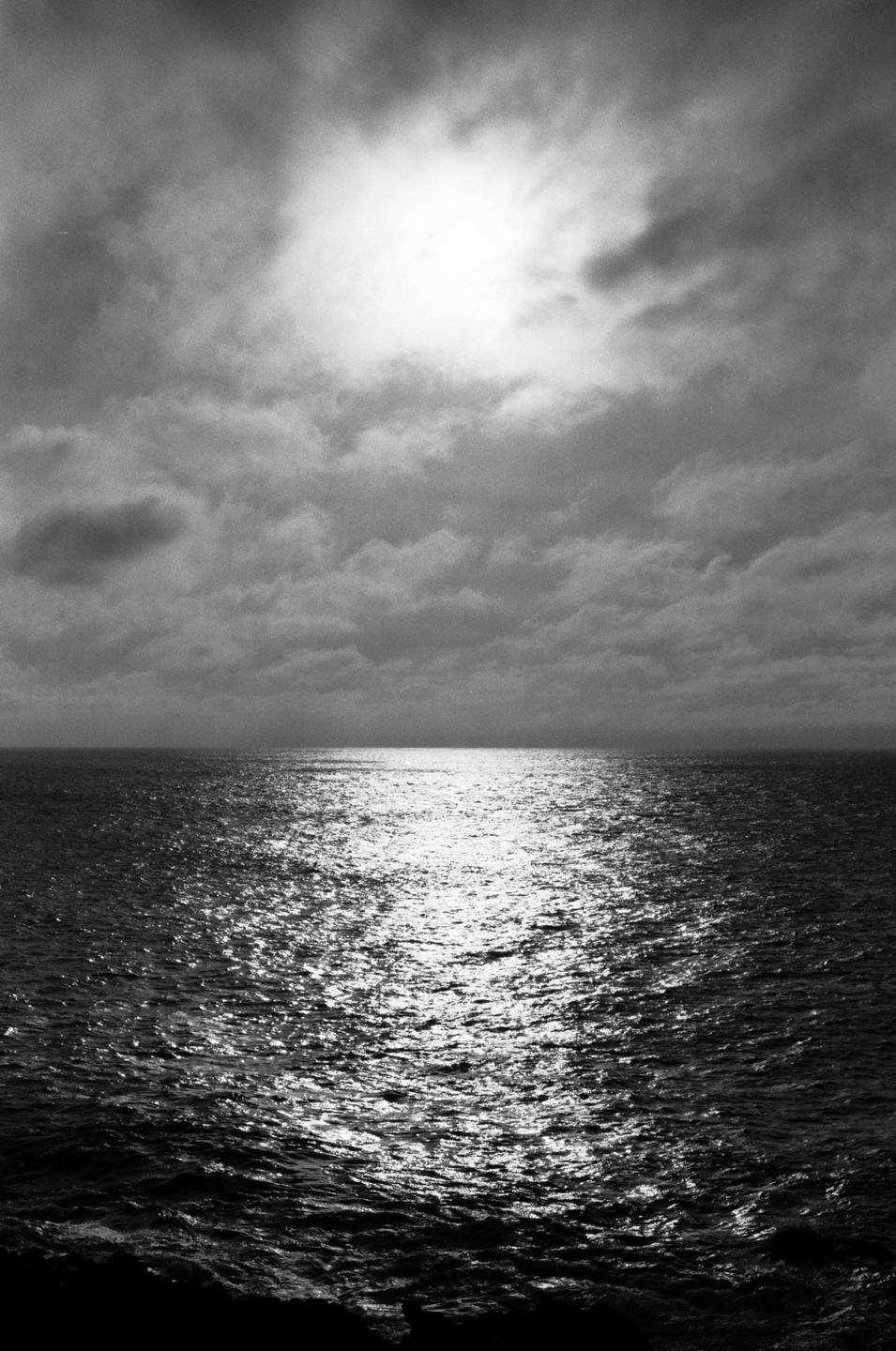 The sun shines through clouds onto a body of water, creating a bright reflection.