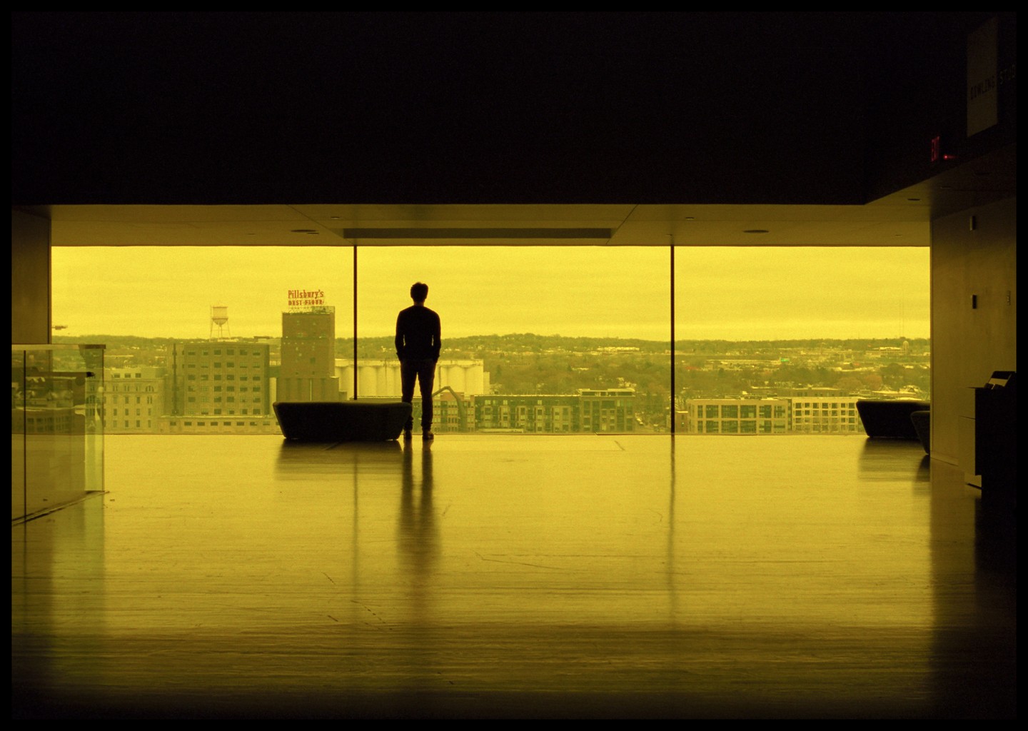 A man stands silhouetted against a large window overlooking a city with a Pillsbury's Best Flour sign visible on a building.