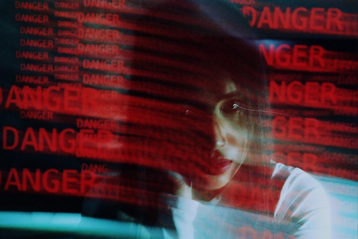 A woman's face is partially obscured by multiple red "DANGER" warnings that appear to be projected onto her.