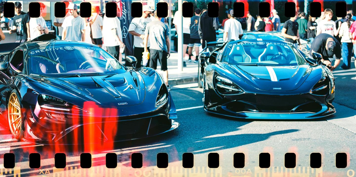 Two supercars are parked on a street with people standing around them.