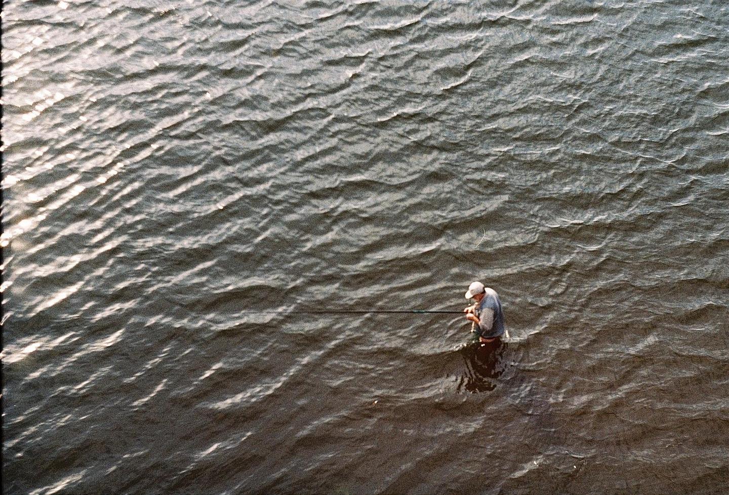 A man stands in the water holding a fishing rod.