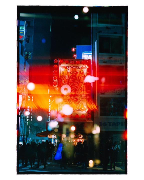 A street at night is filled with people and bright neon signs.