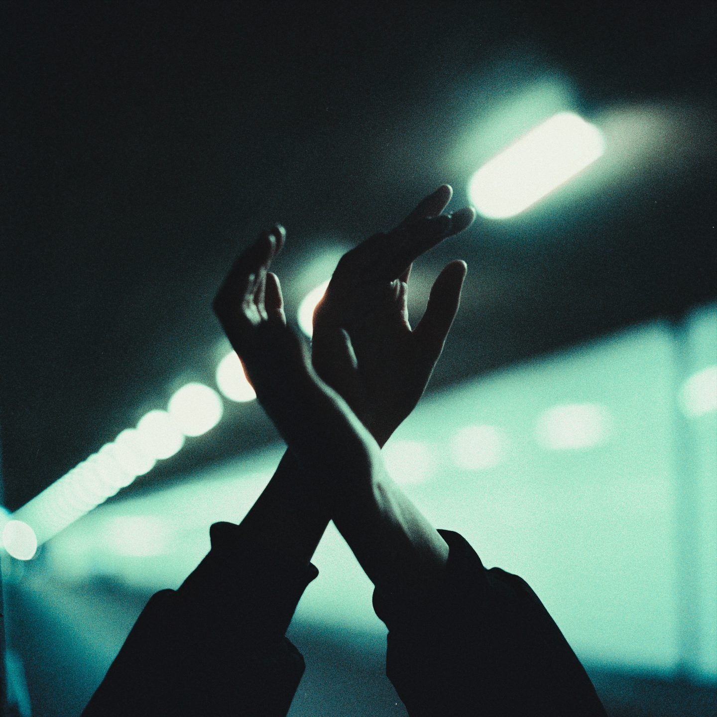 Two hands are silhouetted against a dark background with bright, out-of-focus lights.