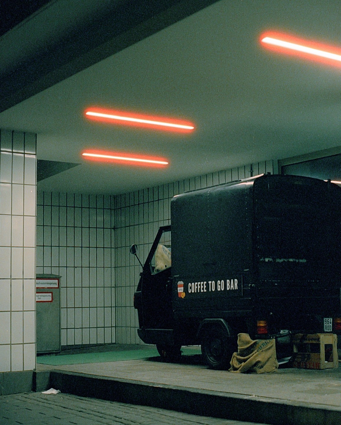 A black coffee to go bar truck is parked under bright orange neon lights in a tiled underpass.