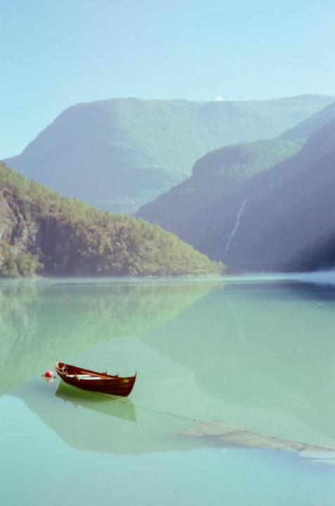 A small wooden boat floats on a calm body of water with mountains in the background.