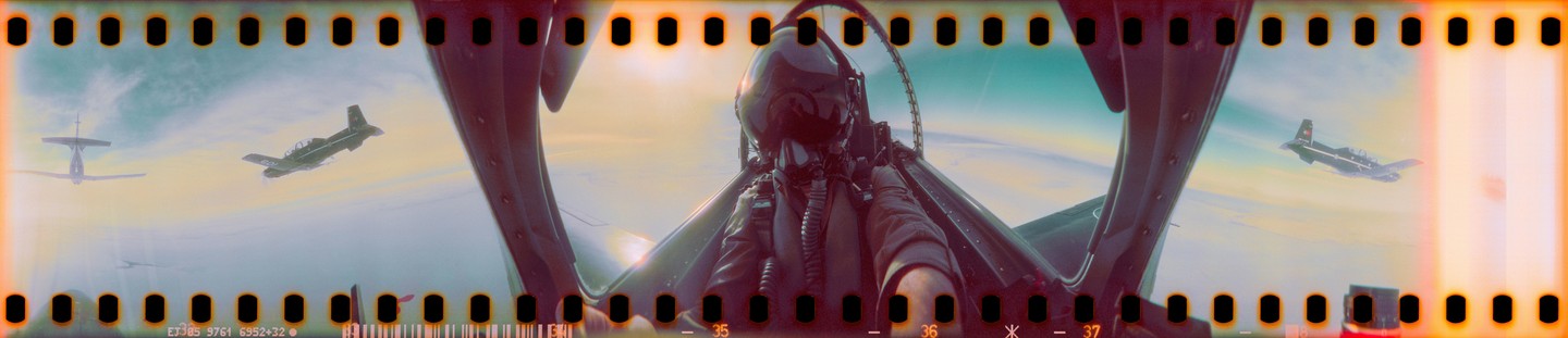A pilot in a cockpit looks out at two other planes flying in formation against a bright sky.