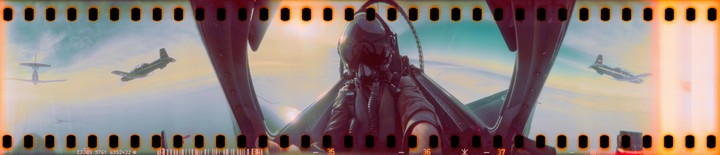 A pilot in a cockpit looks out at two other planes flying in formation against a bright sky.