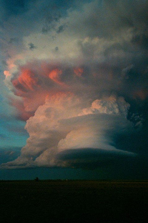 A large, colorful cloud formation dominates the sky above a dark, flat landscape.