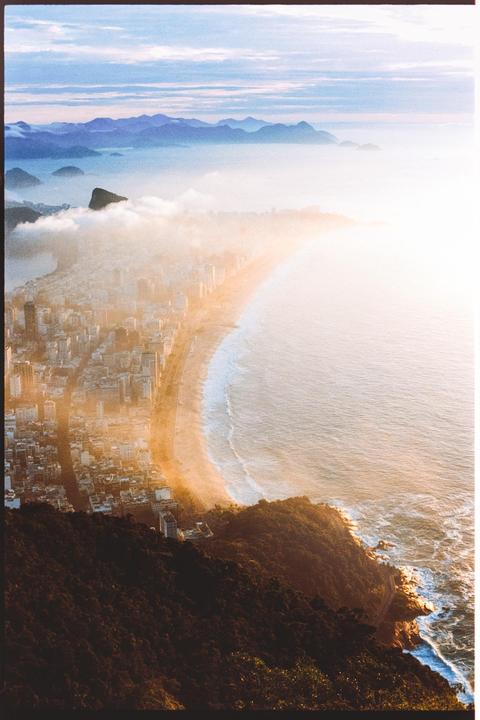A city and beach are visible from a high vantage point, with mountains and clouds in the distance.