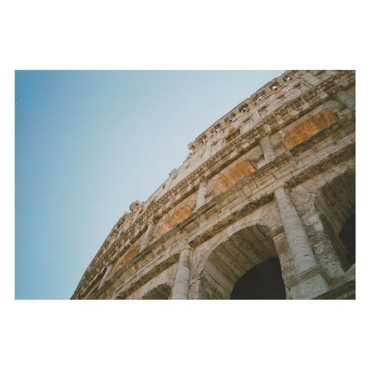 The Colosseum in Rome is viewed from a low angle against a clear sky.