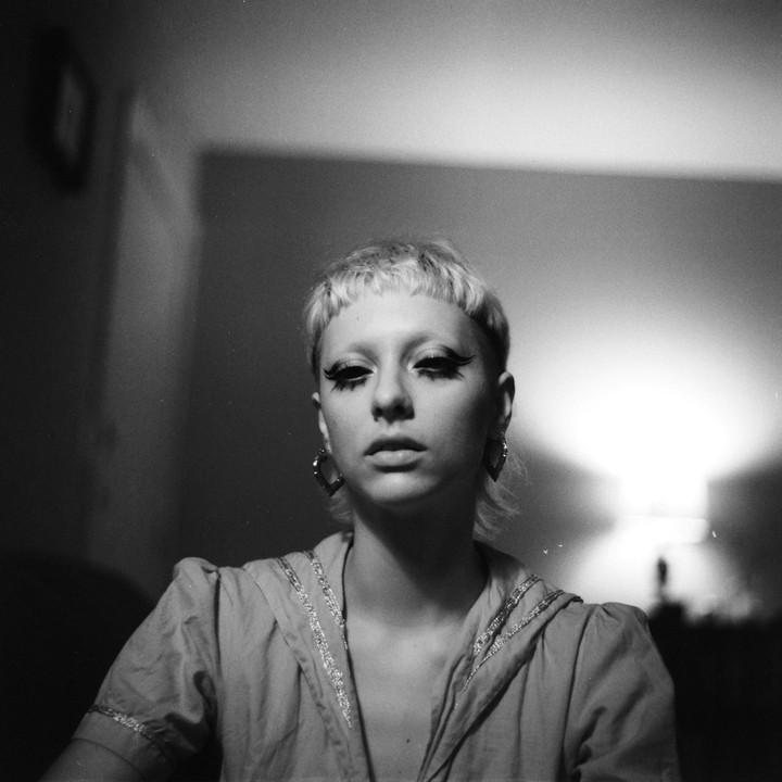 A woman with short hair and dramatic eye makeup looks directly at the viewer.