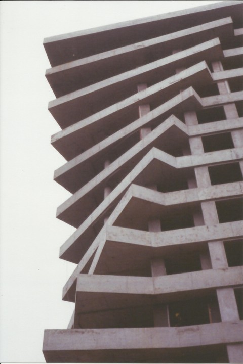 A concrete building with a zig-zagging facade is shown against a plain sky.