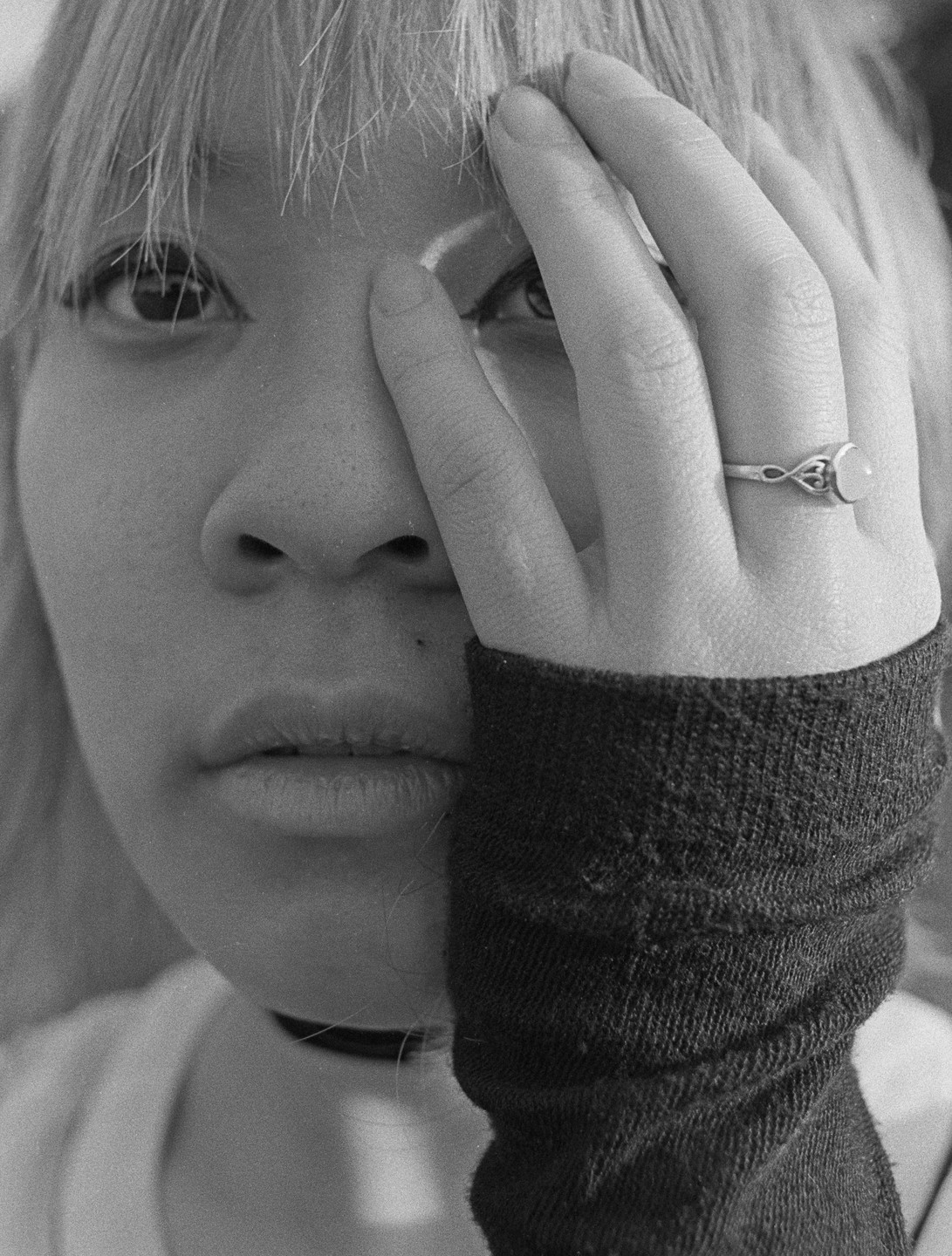 A woman with bangs covers half her face with her hand, revealing one eye and her mouth.