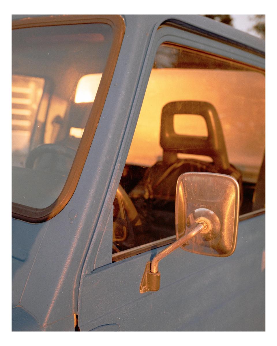 The side of a blue vehicle is visible with a sunset reflected in its windows.