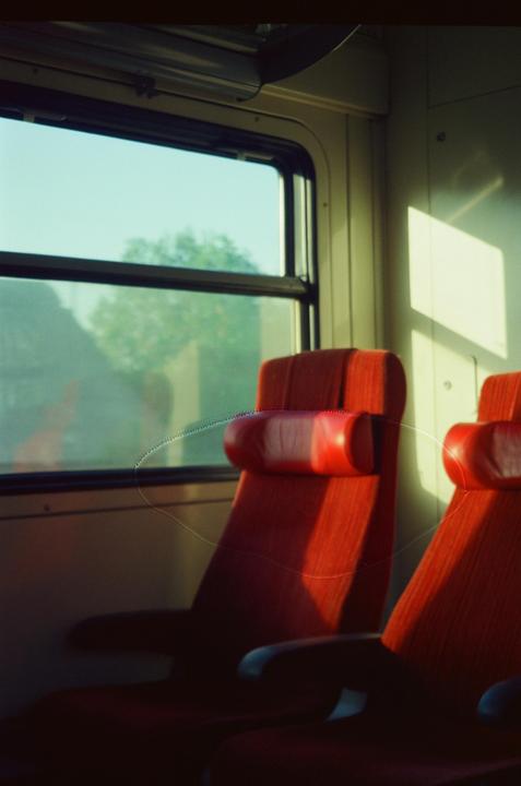 Sunlight streams through a train window, illuminating two red seats and casting shadows on the wall.