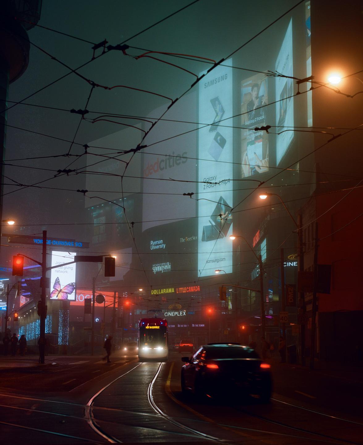 A streetcar and a car drive on a city street at night, with large illuminated billboards in the background.