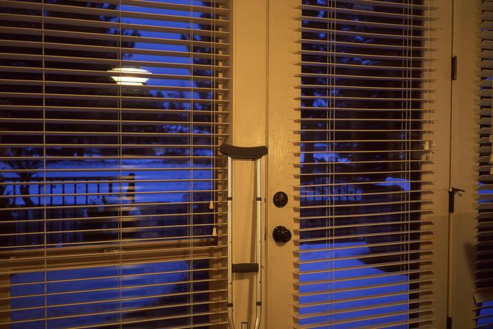 A crutch leans against a door with blinds, revealing a blue outdoor scene with snow and a street light.
