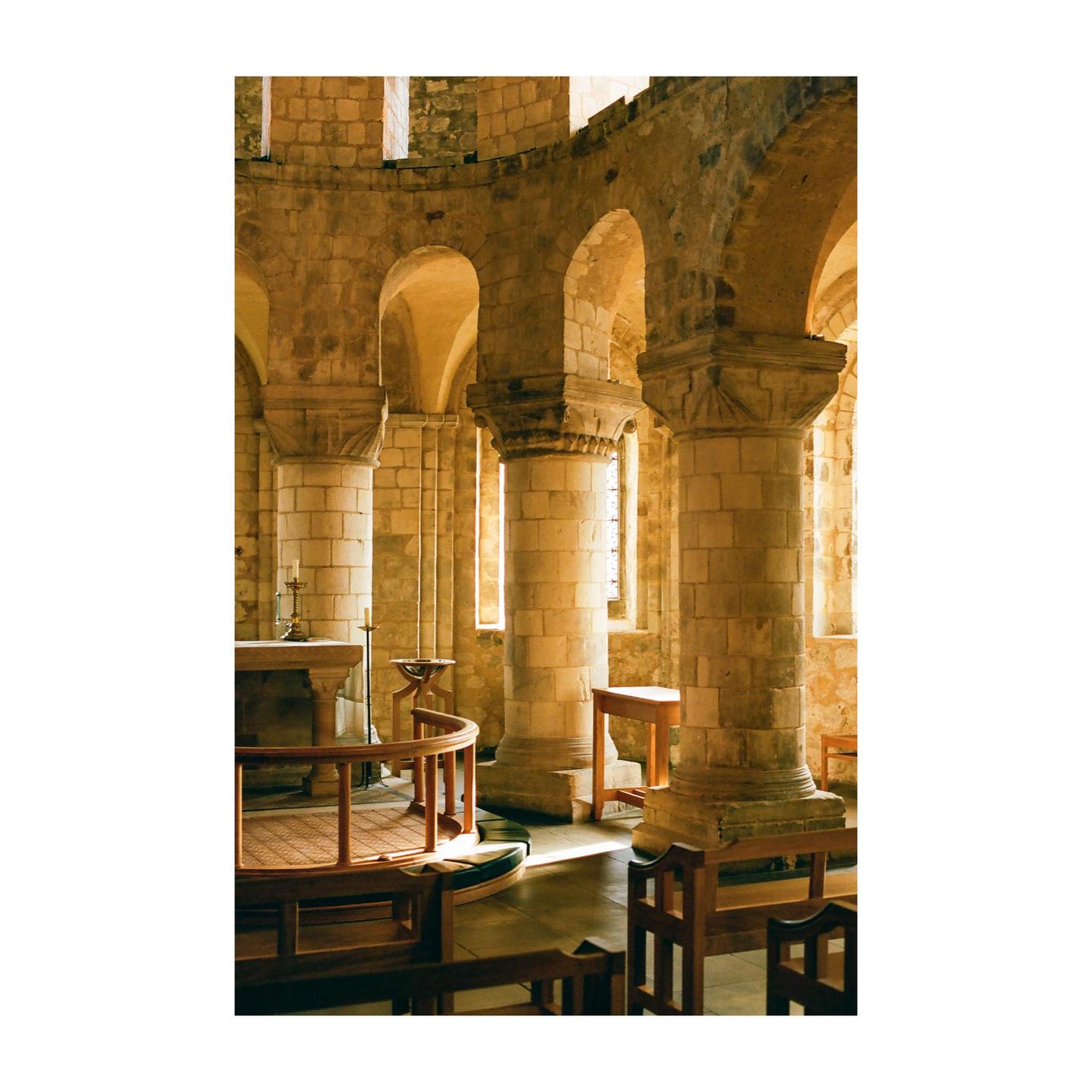 Sunlight streams through windows into a stone church with columns and arches.