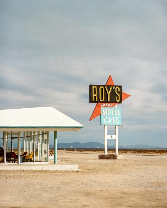 A motel and cafe sign stands next to a building with large windows in a desert landscape.