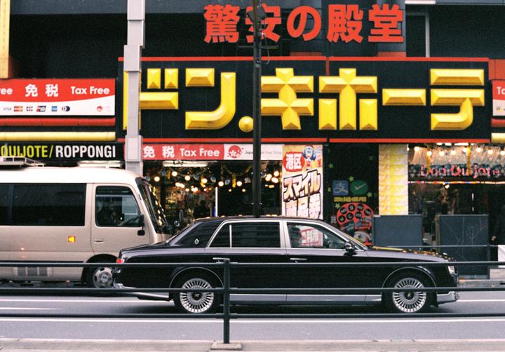 A black Toyota Century car is parked on a street in front of a building with Japanese signs.