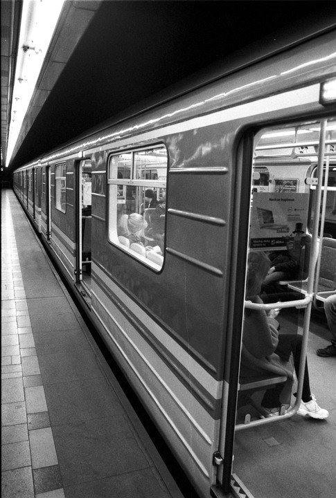A subway train with open doors is stopped at a station platform, with passengers visible inside.
