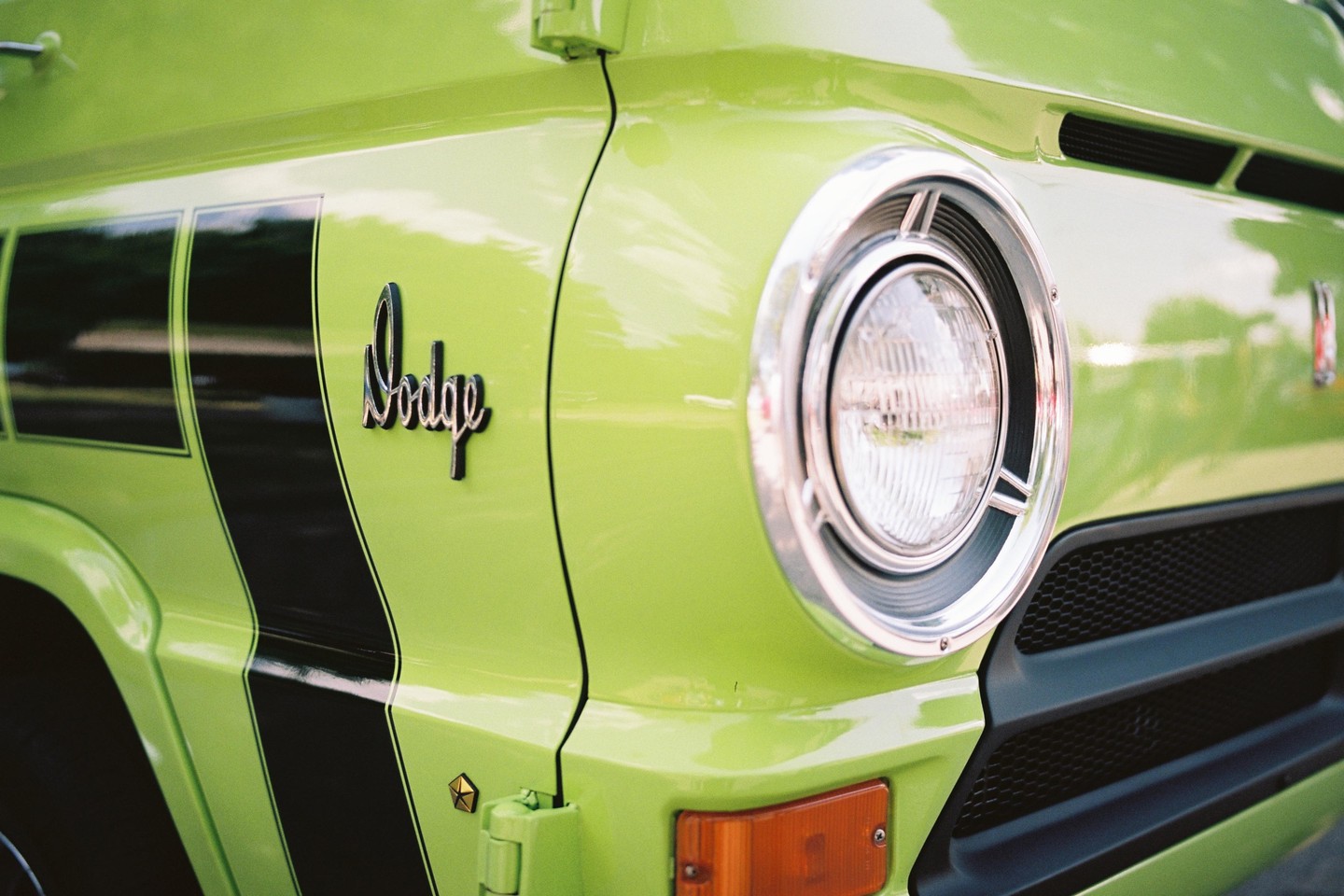 A bright green Dodge van with black racing stripes and a chrome headlight is parked outdoors.