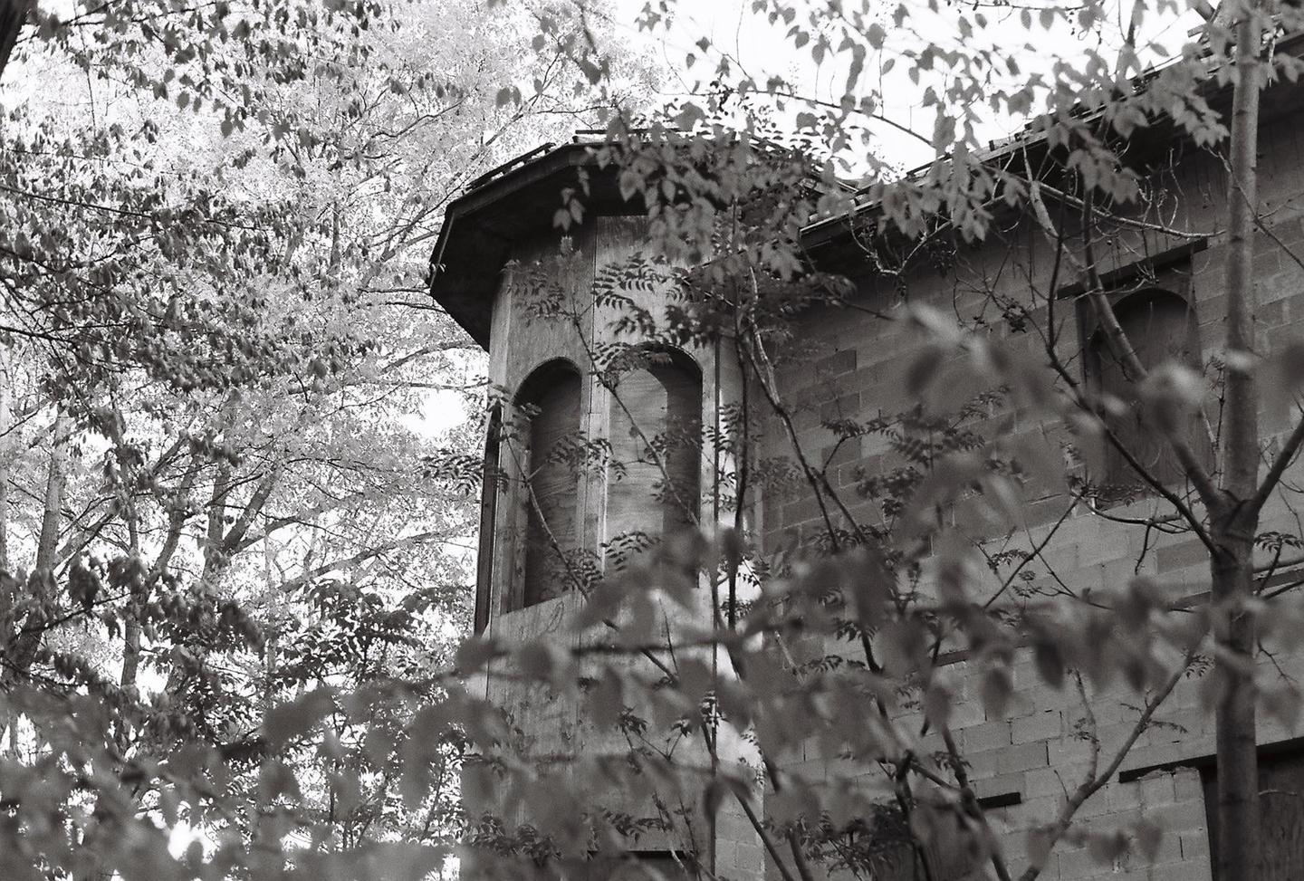 A stone tower with arched windows is partially obscured by tree branches and foliage.