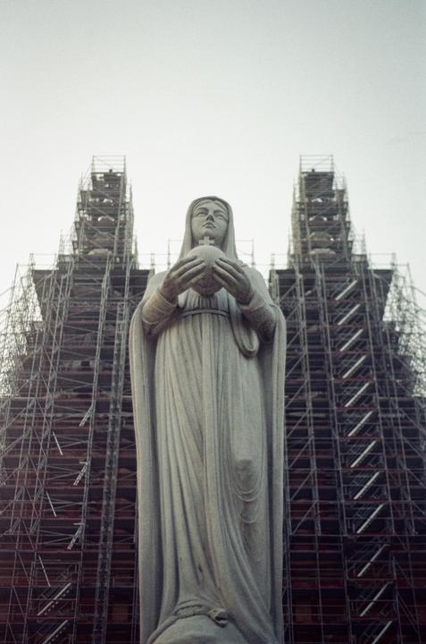 A statue of a woman holding a globe stands in front of a building covered in scaffolding.