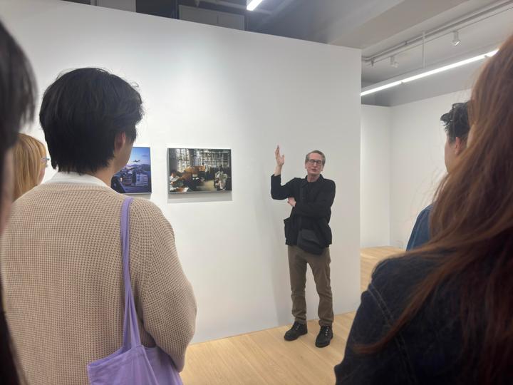 A man gestures while speaking to a small group of people in an art gallery.