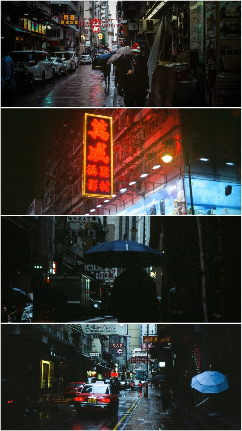 A street in Hong Kong is wet from rain, with neon signs illuminating the buildings and people walking with umbrellas.